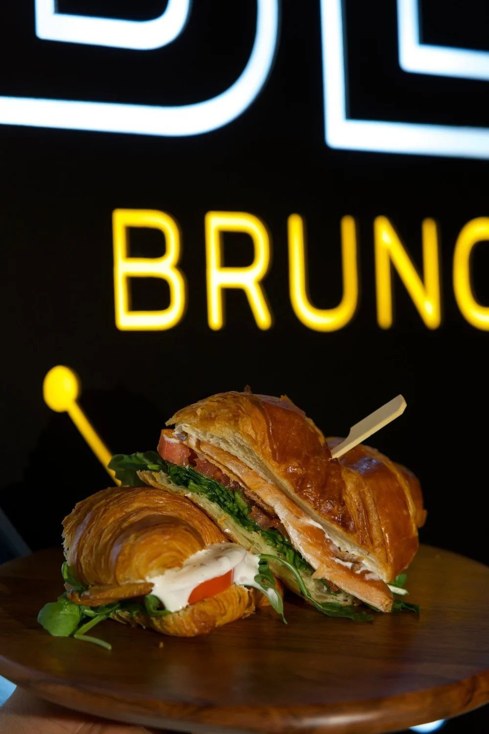 A croissant sandwich in front of a neon brunch sign